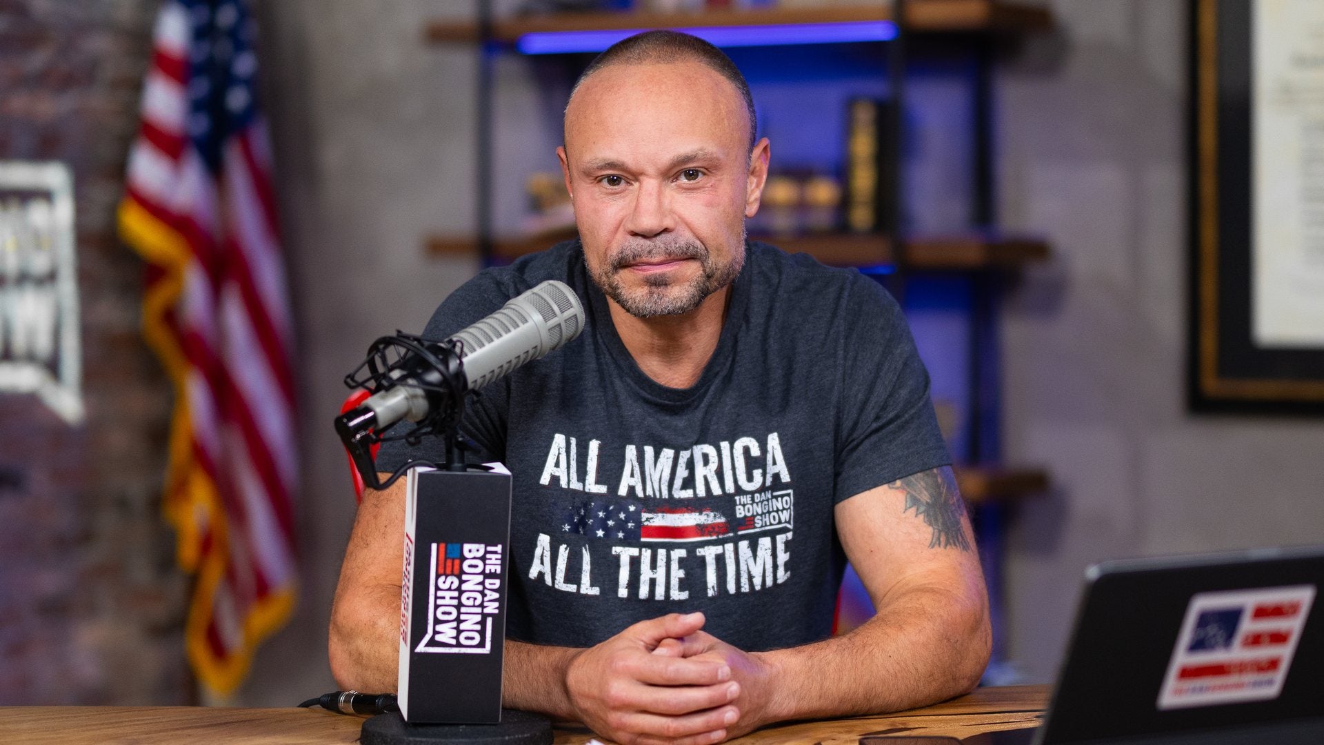 Dan Bongino at the studio desk wearing the All America, All the Time T-shirt